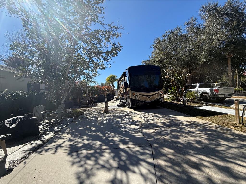 A large motorhome is parked on a concrete driveway next to a house and trees — 124 STALLION LANE, LAKE WALES, FL