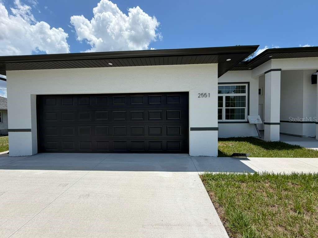 The exterior of a modern house features a black garage door and white stucco walls — 2551 ALHAVEN TERRACE, NORTH PORT, FL