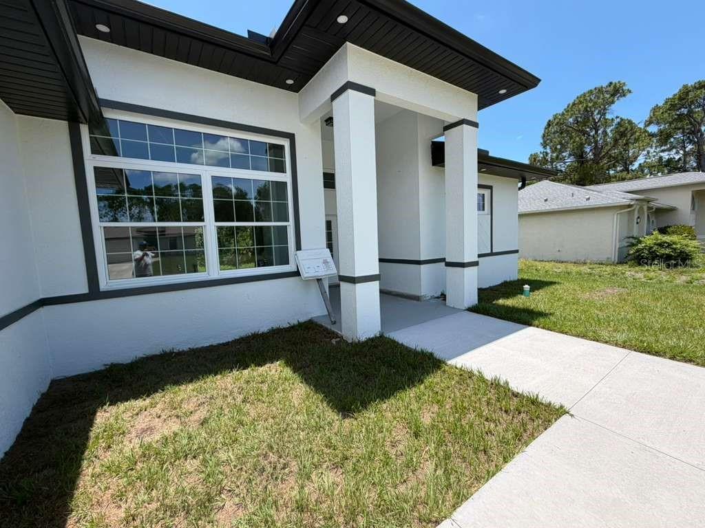 A modern white house exterior features a covered entryway, dark trim, and a concrete walkway — 2551 ALHAVEN TERRACE, NORTH PORT, FL