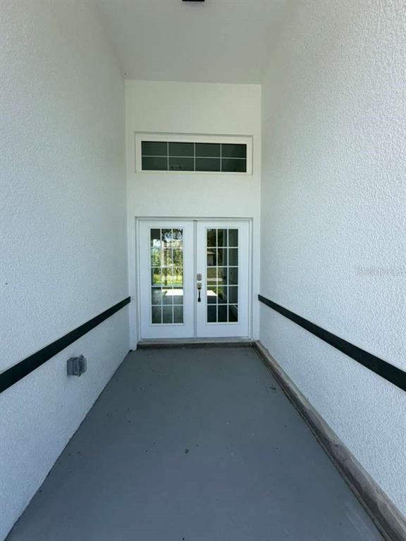A covered entryway features white stucco walls, a gray concrete floor, and white double doors — 2551 ALHAVEN TERRACE, NORTH PORT, FL