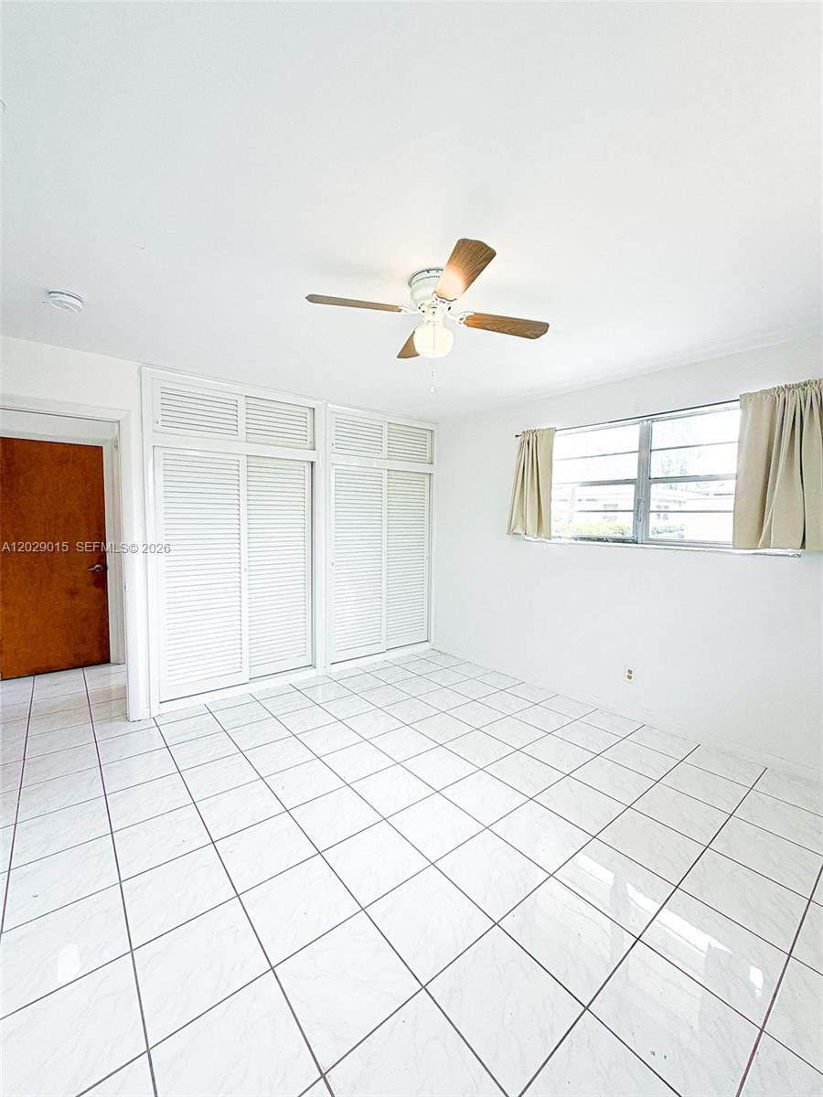 A bedroom features white tiled floors, a ceiling fan, and white louvered closet doors — 1401 Grant St # 3, Hollywood FL 33020, HOLLYWOOD, FL
