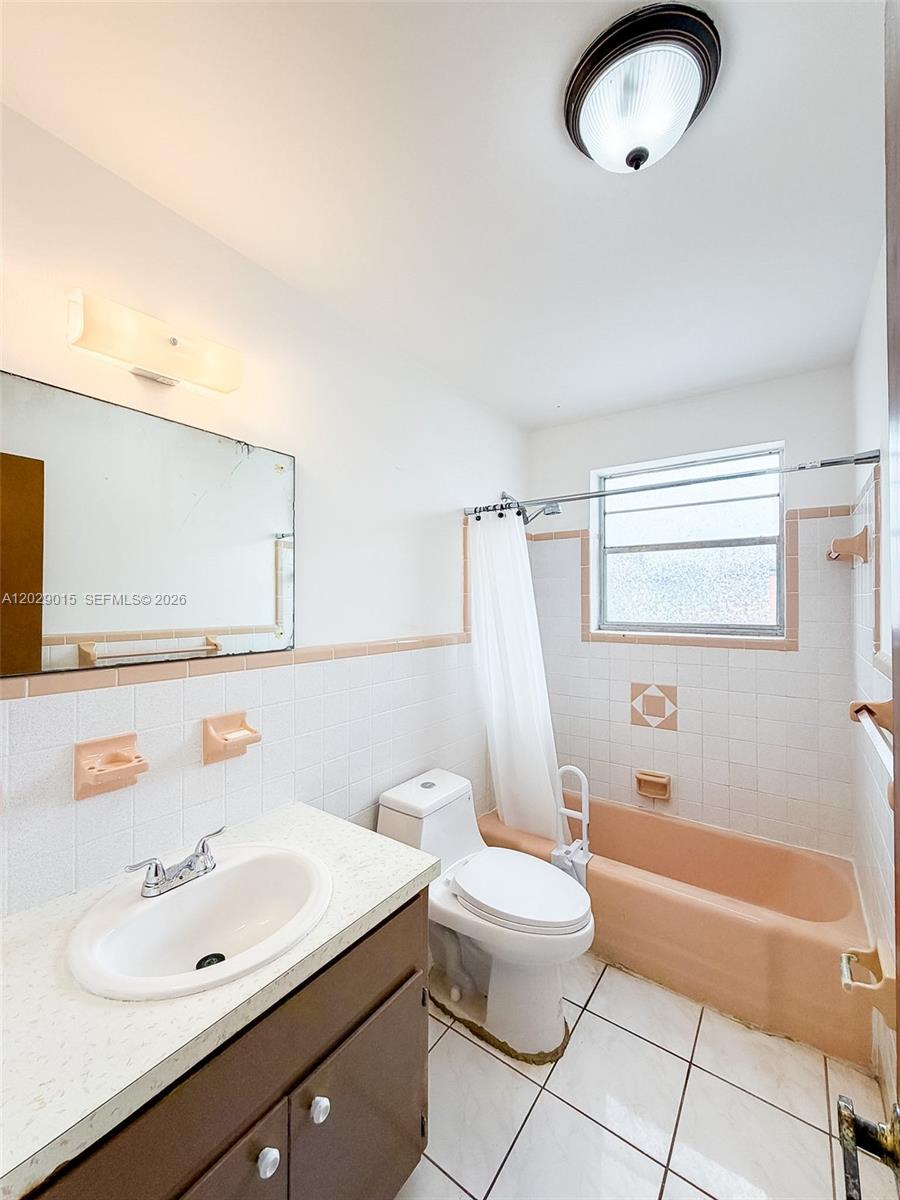 A bathroom features a vanity, a toilet, and a peach-colored bathtub with tiled walls — 1401 Grant St # 3, Hollywood FL 33020, HOLLYWOOD, FL
