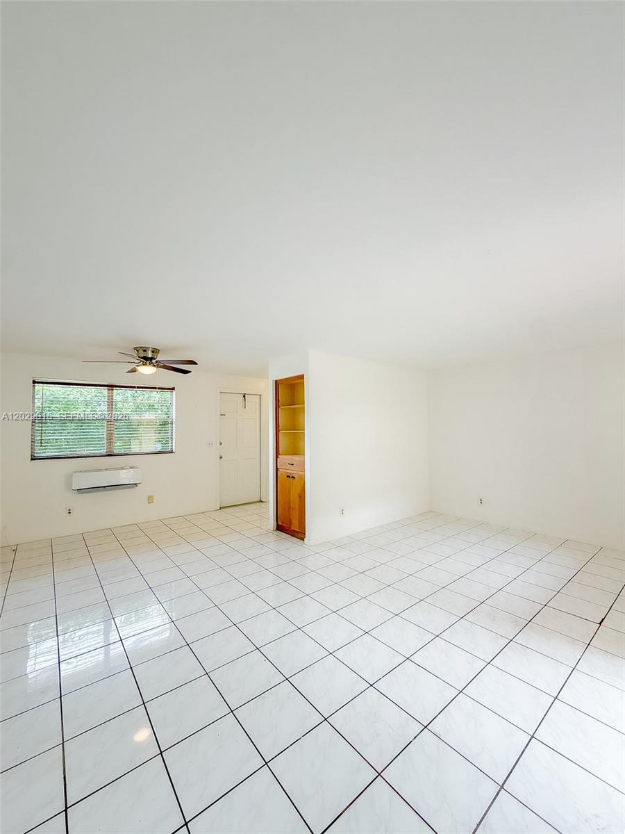 An empty room features white tiled floors, a ceiling fan, and a built-in wooden cabinet — 1401 Grant St # 3, Hollywood FL 33020, HOLLYWOOD, FL
