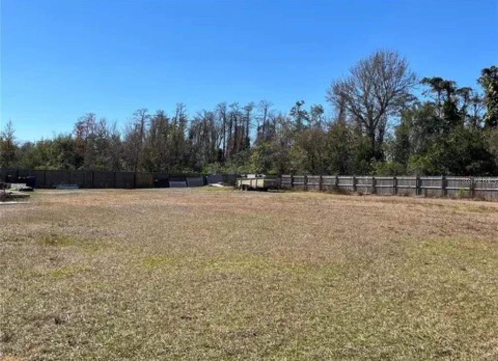 A large, flat, grassy lot enclosed by a wooden fence with trees in the background — 652 MADRID DRIVE, KISSIMMEE, FL