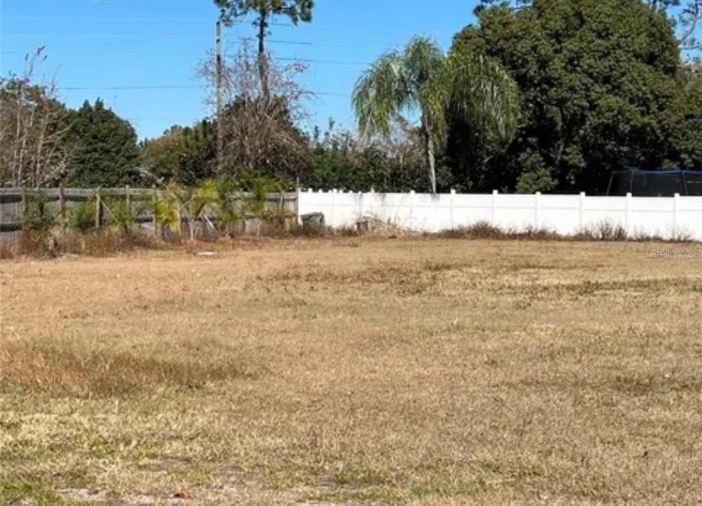 A flat, grassy vacant lot features a white vinyl fence and trees in the background — 652 MADRID DRIVE, KISSIMMEE, FL