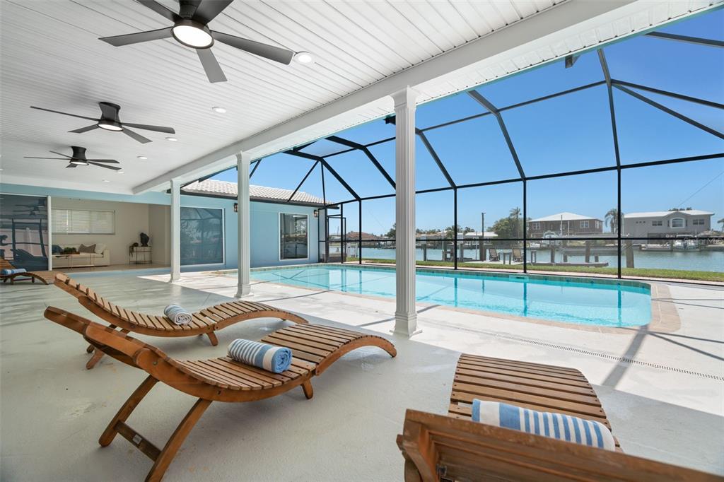 A covered patio with lounge chairs overlooks a screened-in swimming pool and a canal — 11900 7TH STREET E, TREASURE ISLAND, FL