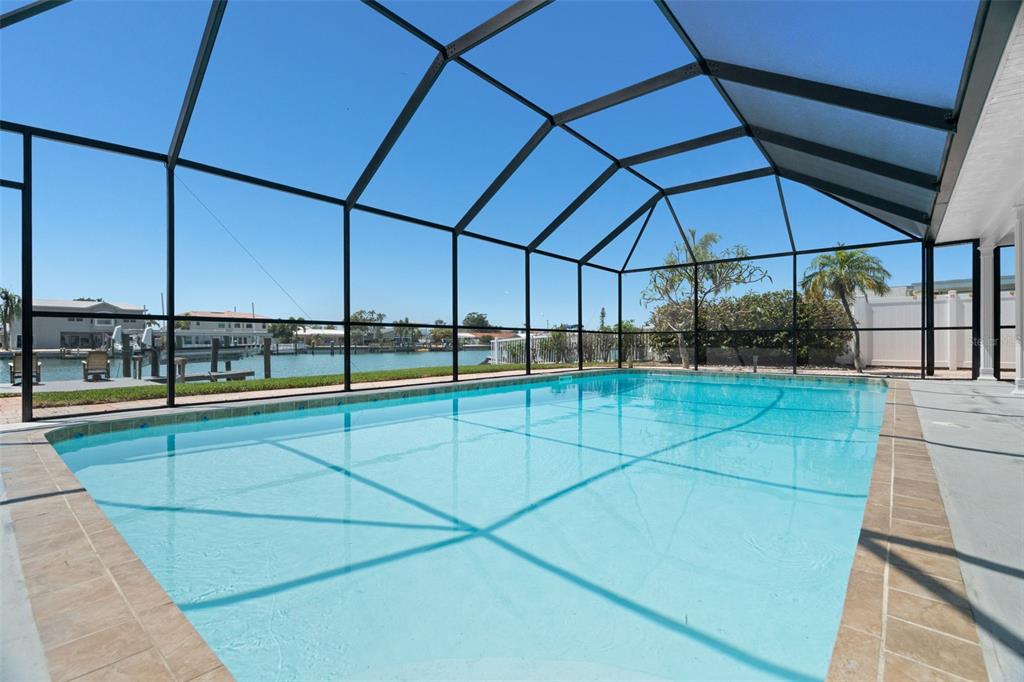 A swimming pool enclosed by a screened lanai overlooks a canal with nearby houses — 11900 7TH STREET E, TREASURE ISLAND, FL