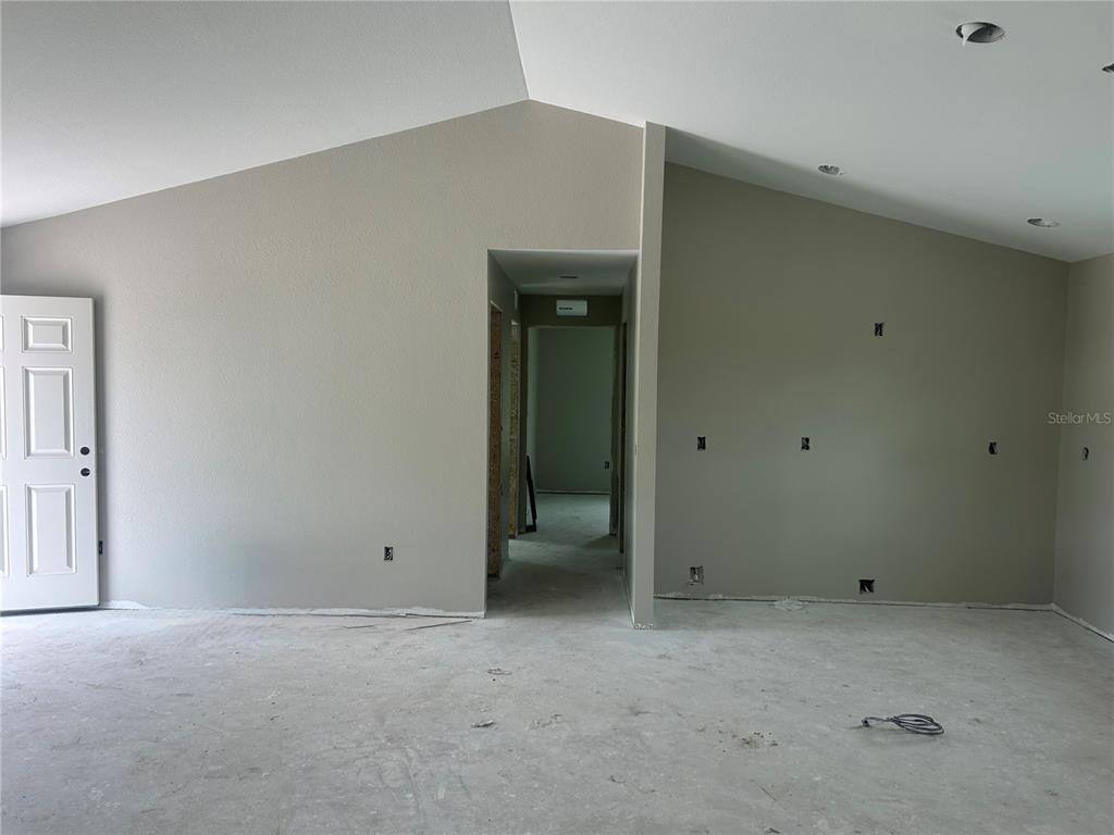 An unfinished room features vaulted ceilings, beige walls, and a doorway leading to a hallway — 11506 SW LEMON AVENUE, ARCADIA, FL