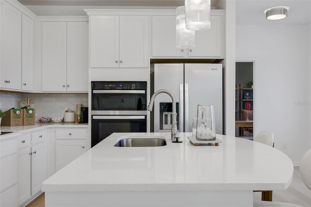 A modern kitchen features white cabinetry, a quartz-topped island with a sink, and stainless appliances — 35 BIG PINE DRIVE, PALM COAST, FL