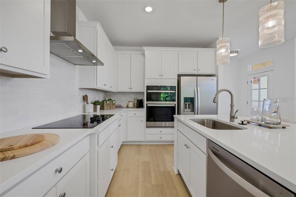 A modern white kitchen features stainless steel appliances, quartz countertops, and light wood flooring — 35 BIG PINE DRIVE, PALM COAST, FL