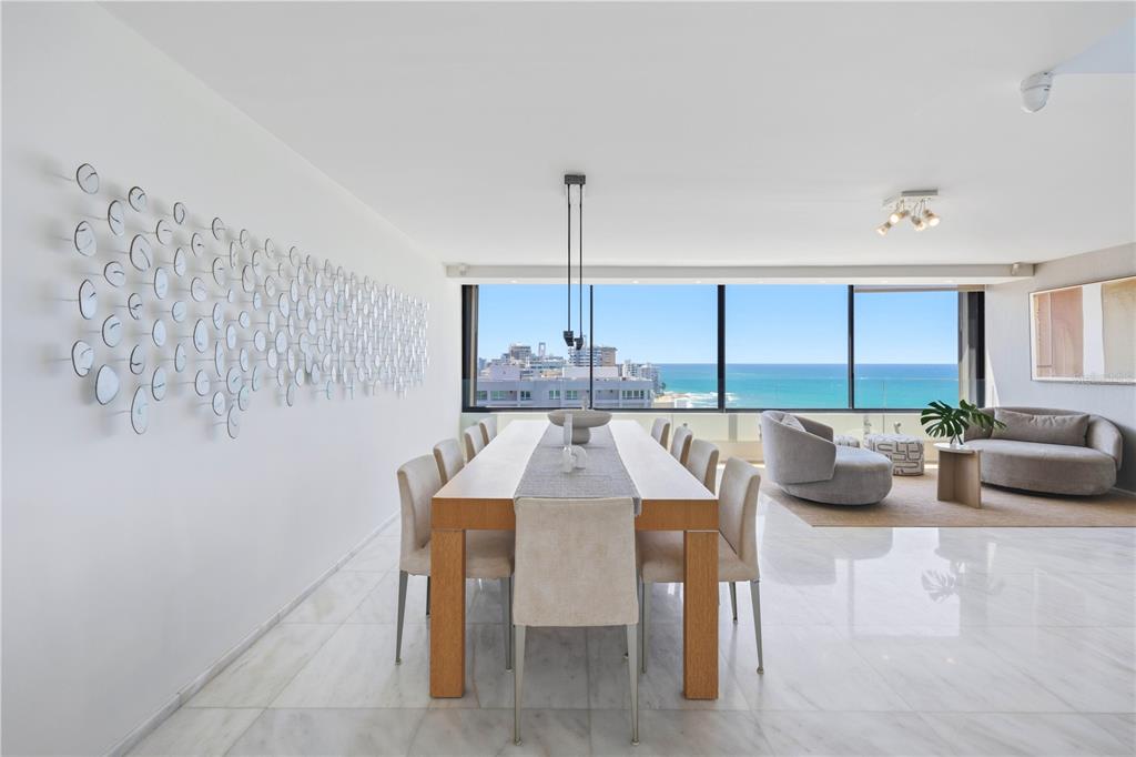 A dining room with a long wooden table, marble floors, and a large ocean-view window — 1 TAFT STREET UNIT Penthouse-C, SAN JUAN, PR