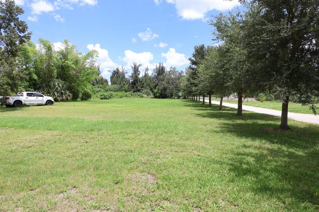 A grassy lot features a white pickup truck and a row of trees along a driveway — 3250 TAYLOR ROAD, PUNTA GORDA, FL