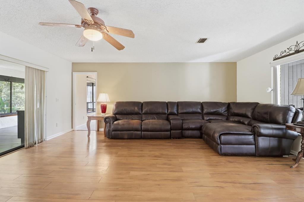 A living room features a large brown leather sectional, wood-look flooring, and a ceiling fan — 98 SYCAMORE CIRCLE, HOMOSASSA, FL