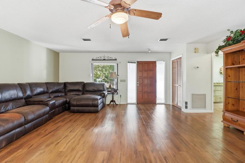 A living room features a brown leather sectional, wood-look flooring, and a ceiling fan — 98 SYCAMORE CIRCLE, HOMOSASSA, FL