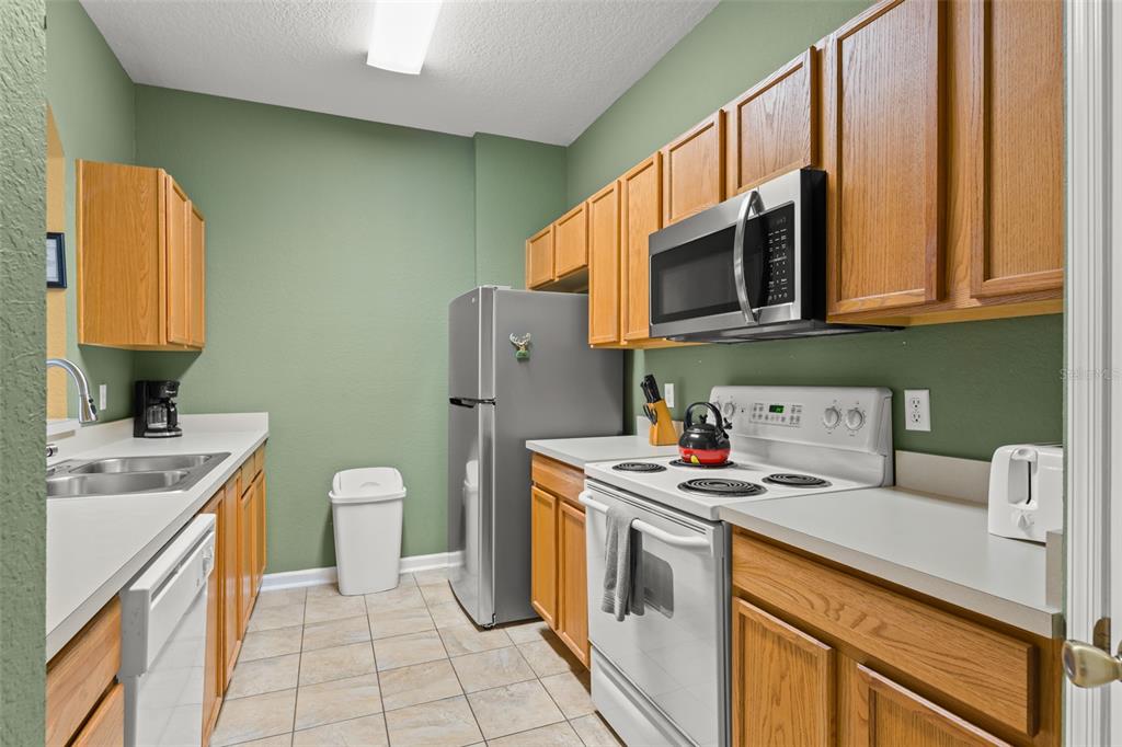 A galley kitchen features light wood cabinets, green walls, tile flooring, and stainless steel appliances — 7675 COMROW STREET UNIT 405, KISSIMMEE, FL