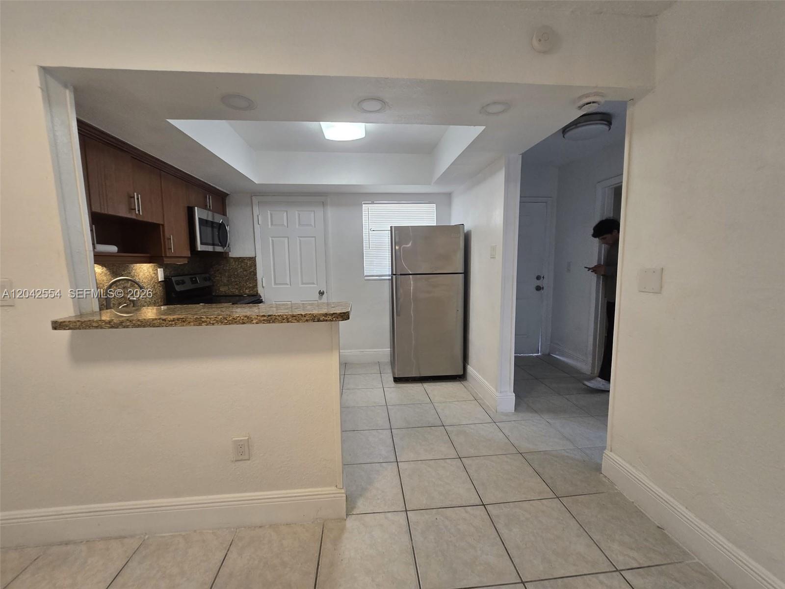 A kitchen features wood cabinets, granite countertops, stainless steel appliances, and light-colored tile flooring — 2441 NW 13th St # 62, Miami FL 33125, MIAMI, FL