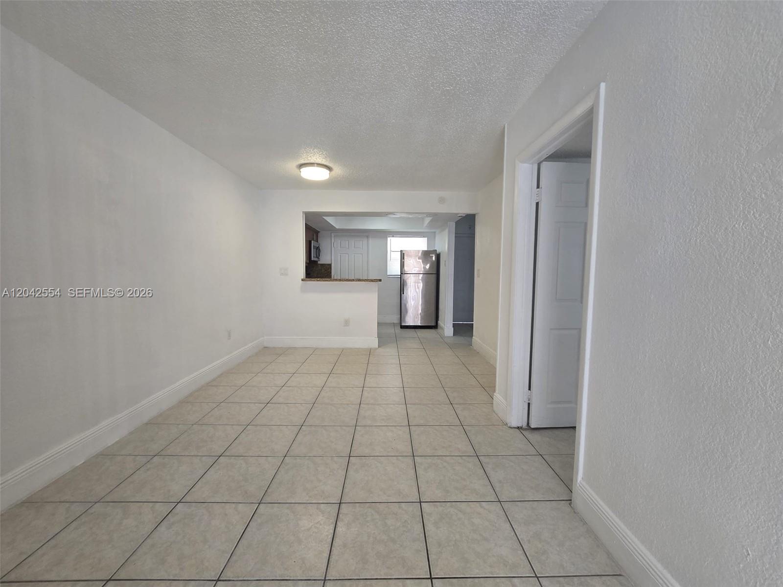 A room with light-colored tile flooring leads to a kitchen area with stainless steel appliances — 2441 NW 13th St # 62, Miami FL 33125, MIAMI, FL