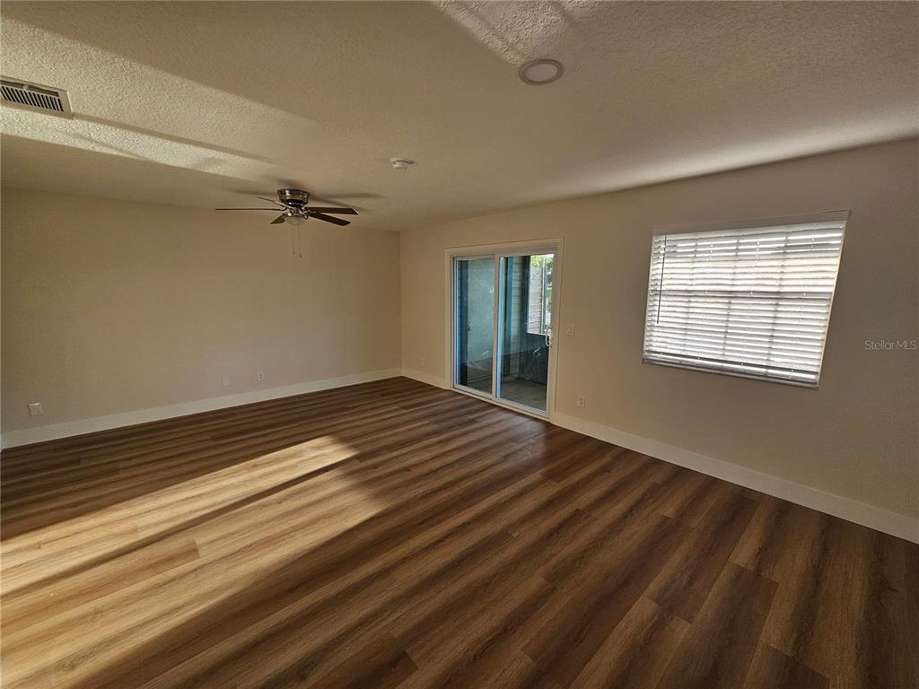 An empty living room features wood-look flooring, a ceiling fan, and sliding glass patio doors — 11730 WHITEWING COURT, ORLANDO, FL