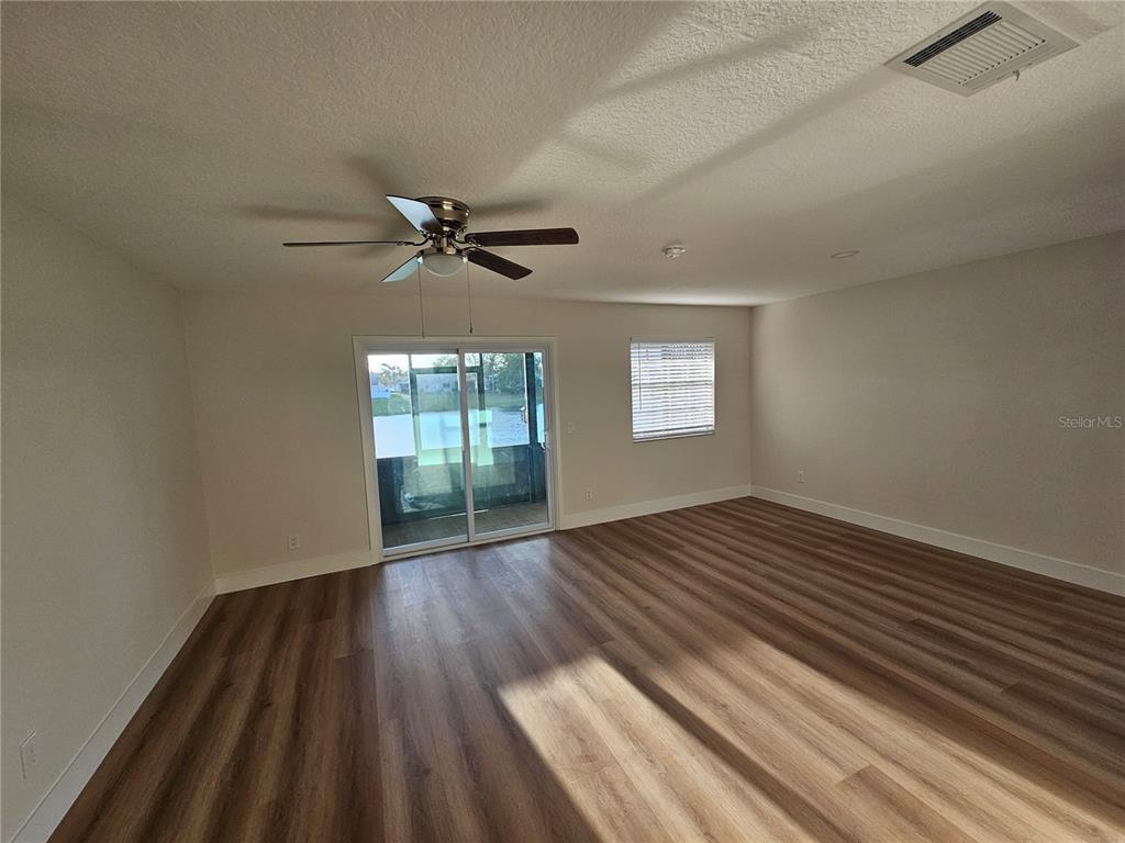 An empty room features wood-look flooring, a ceiling fan, a sliding glass door, and windows — 11730 WHITEWING COURT, ORLANDO, FL
