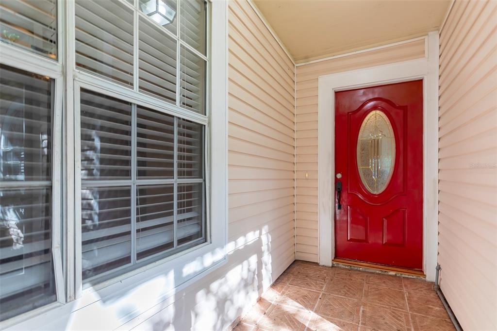 A red front door with an oval glass insert sits on a tiled porch — 824 HILLARY COURT, LONGWOOD, FL