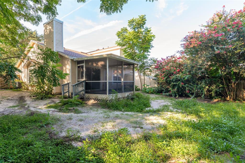A beige house with a screened-in porch and a large, overgrown backyard with flowering trees — 824 HILLARY COURT, LONGWOOD, FL