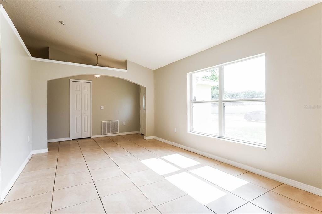 A bright room features beige tile flooring, an arched entryway, and a large window — 2807 ARBOUR TRAIL COURT, DELTONA, FL