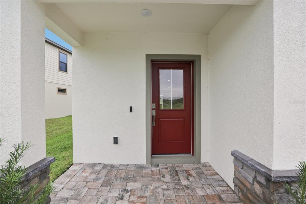 A red front door with a glass pane sits under a covered porch with pavers — 3255 CUP DRIVE, LAKELAND, FL