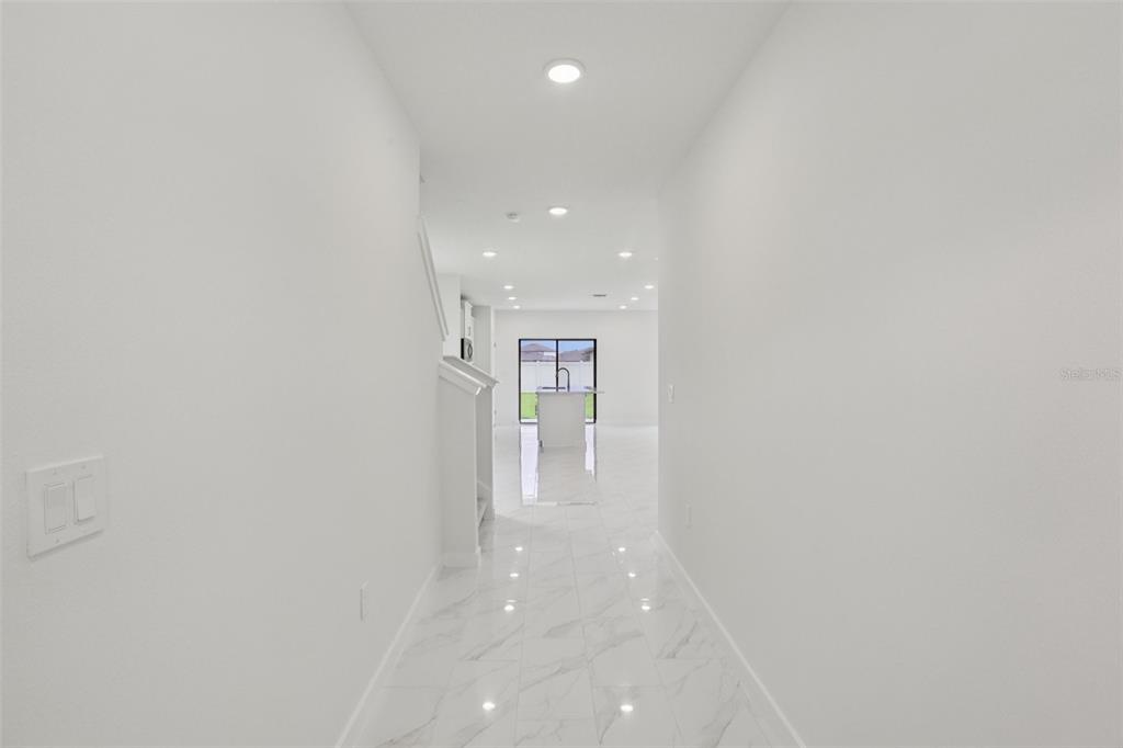 A bright hallway with white walls and light-colored marble-style tile flooring leads to a kitchen — 3255 CUP DRIVE, LAKELAND, FL