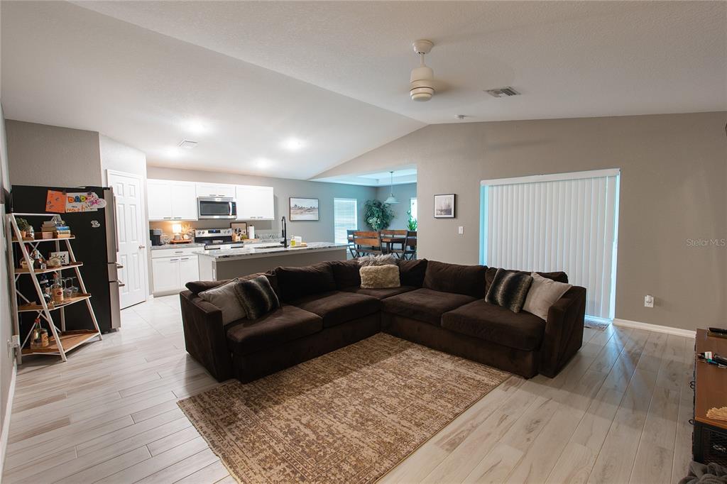 An open-concept living room with a large brown sectional sofa, rug, and kitchen area — 3715 TEAKWOOD STREET, FORT MYERS, FL