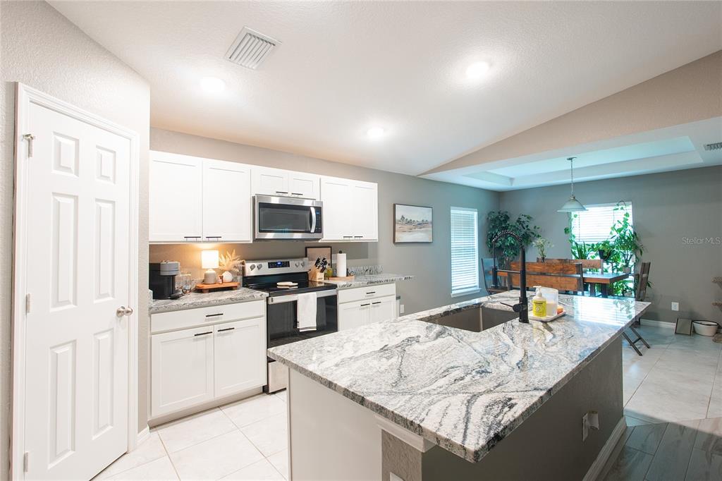 A kitchen with white cabinets, granite countertops, a center island, and an adjacent dining area — 3715 TEAKWOOD STREET, FORT MYERS, FL