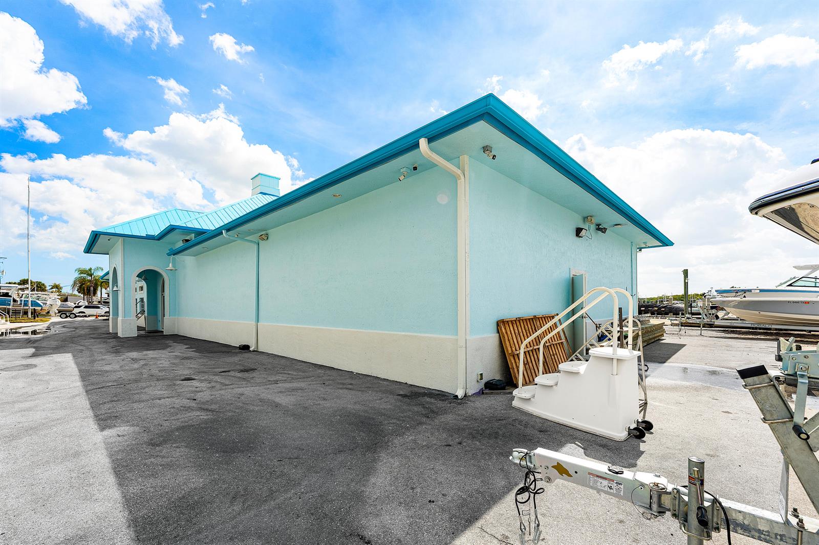A light blue building with a metal roof stands in a paved boat storage yard — 250 SW Monterey Road, Stuart FL 34994, STUART, FL