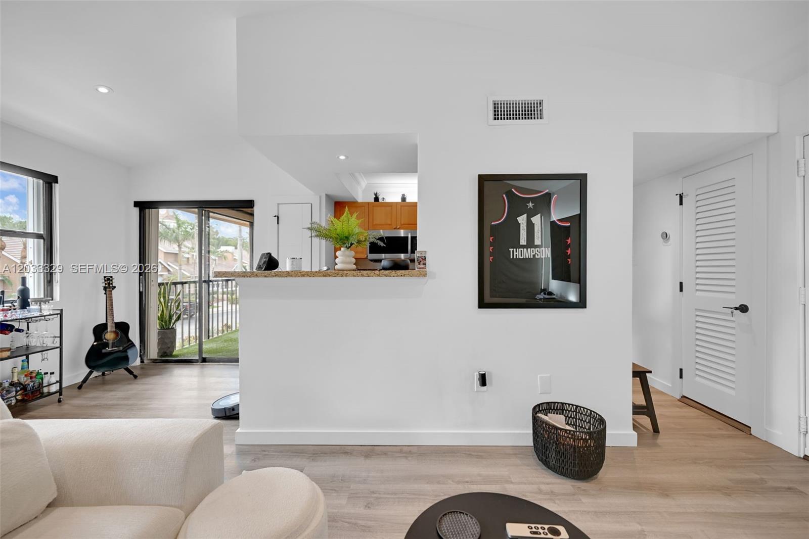 A living room features light wood flooring, a kitchen pass-through, and a framed basketball jersey — 10560 SW 156th Pl # 208, Miami FL 33196, MIAMI, FL