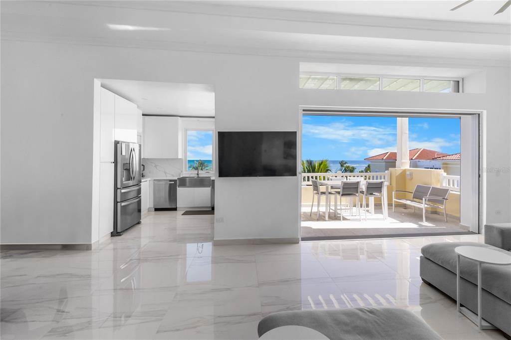 A bright living room with white marble floors opens to a balcony overlooking the ocean — 400 OCEAN DRIVE UNIT 453, HUMACAO, PR