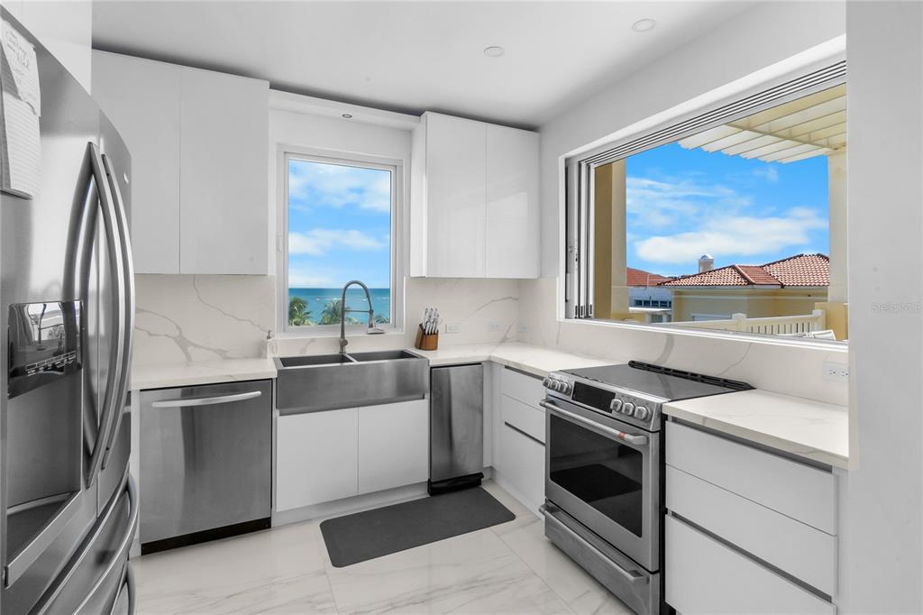 A modern white kitchen features stainless steel appliances, marble countertops, and a view of the ocean — 400 OCEAN DRIVE UNIT 453, HUMACAO, PR