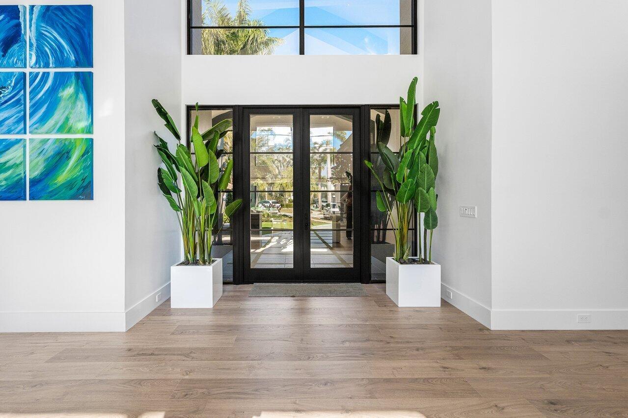 A bright entryway features light wood flooring, two large potted plants, and black-framed glass doors — 3746 NW 53rd Street, Boca Raton FL 33496, BOCA RATON, FL