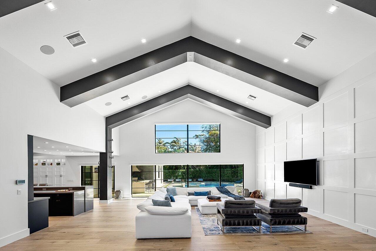 A spacious living room features vaulted ceilings with dark beams, white paneling, and pool views — 3746 NW 53rd Street, Boca Raton FL 33496, BOCA RATON, FL