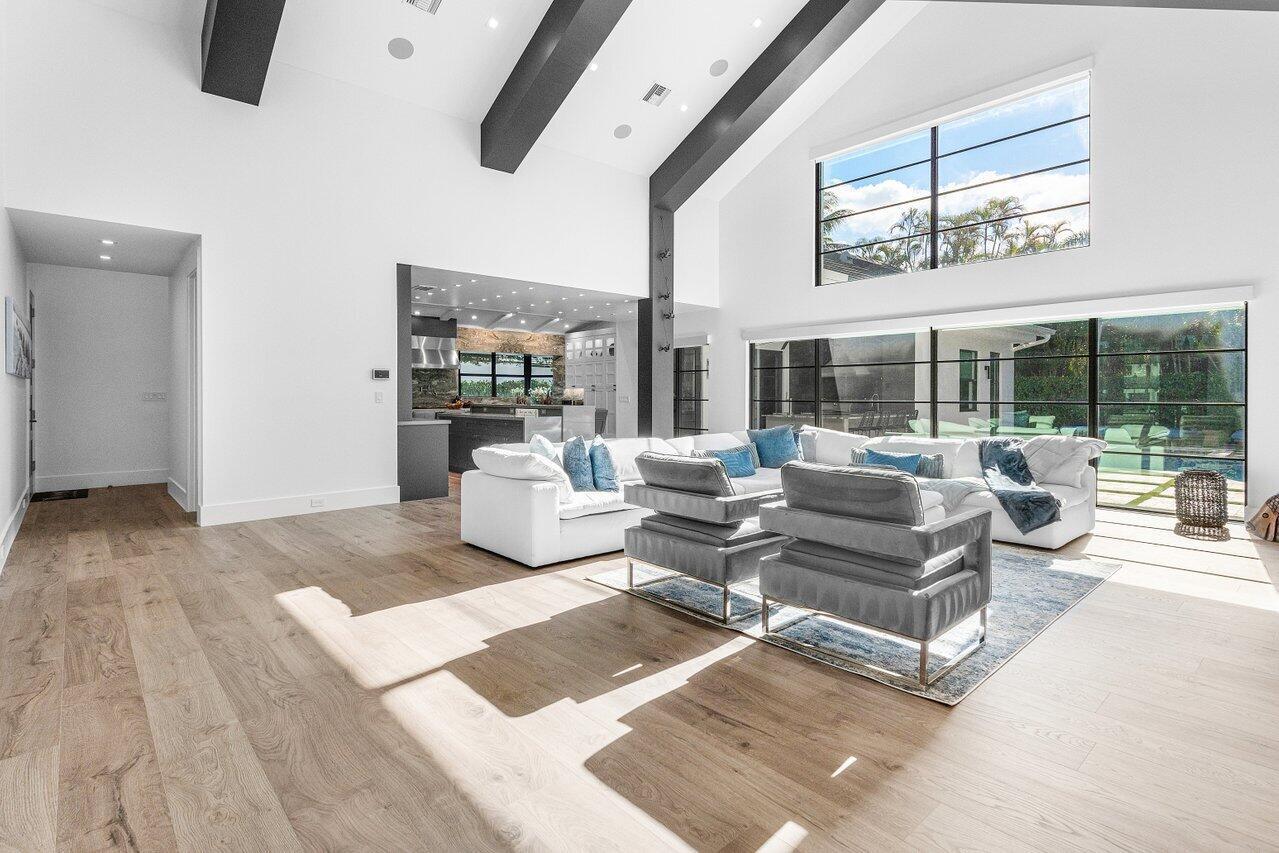 A bright living room features vaulted ceilings, dark beams, white walls, and large glass windows — 3746 NW 53rd Street, Boca Raton FL 33496, BOCA RATON, FL