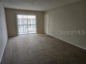 An empty living room with beige carpet, light-colored walls, and a sliding glass balcony door — 5331 SUMMERLIN ROAD UNIT 3112, FORT MYERS, FL