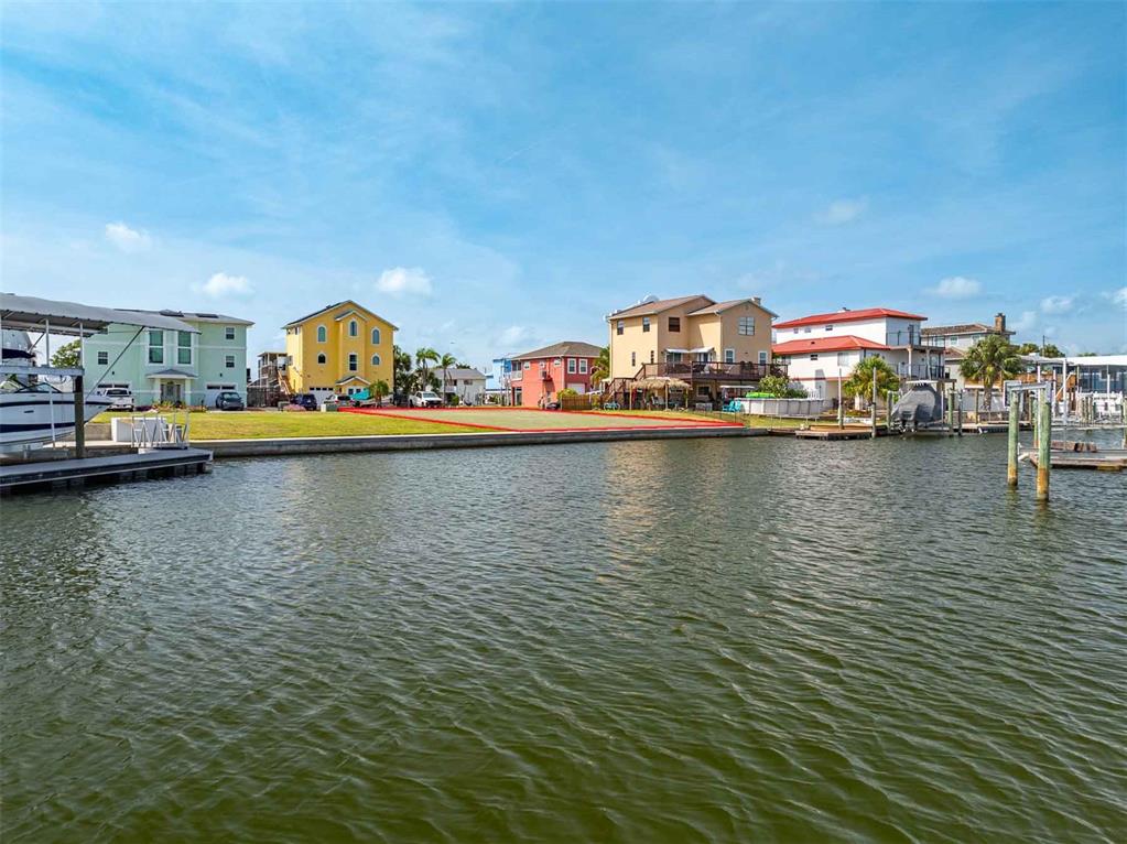 A vacant waterfront lot sits between several houses along a canal under a blue sky — 6520 LOUISE COURT, HUDSON, FL