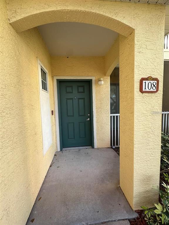 A green front door is set within a covered, yellow stucco entryway marked number 108 — 12220 WILD IRIS WAY UNIT 108, ORLANDO, FL