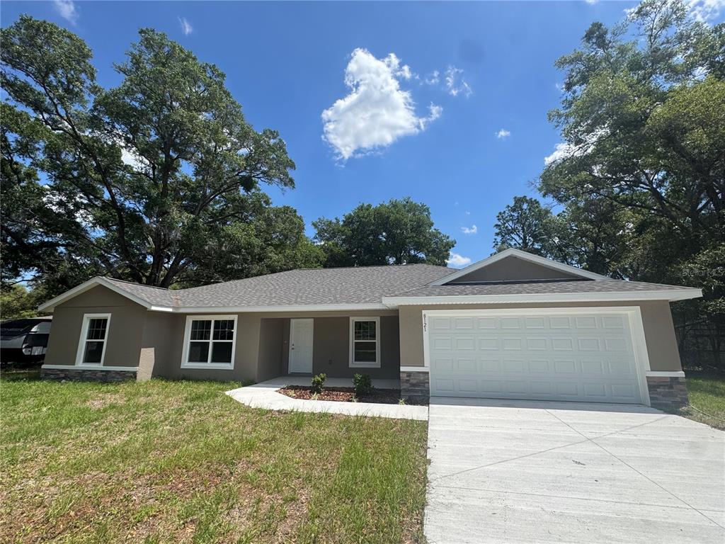 A single-story house with a tan exterior, white garage door, and a concrete driveway — 8121 SW 202ND TERRACE, DUNNELLON, FL