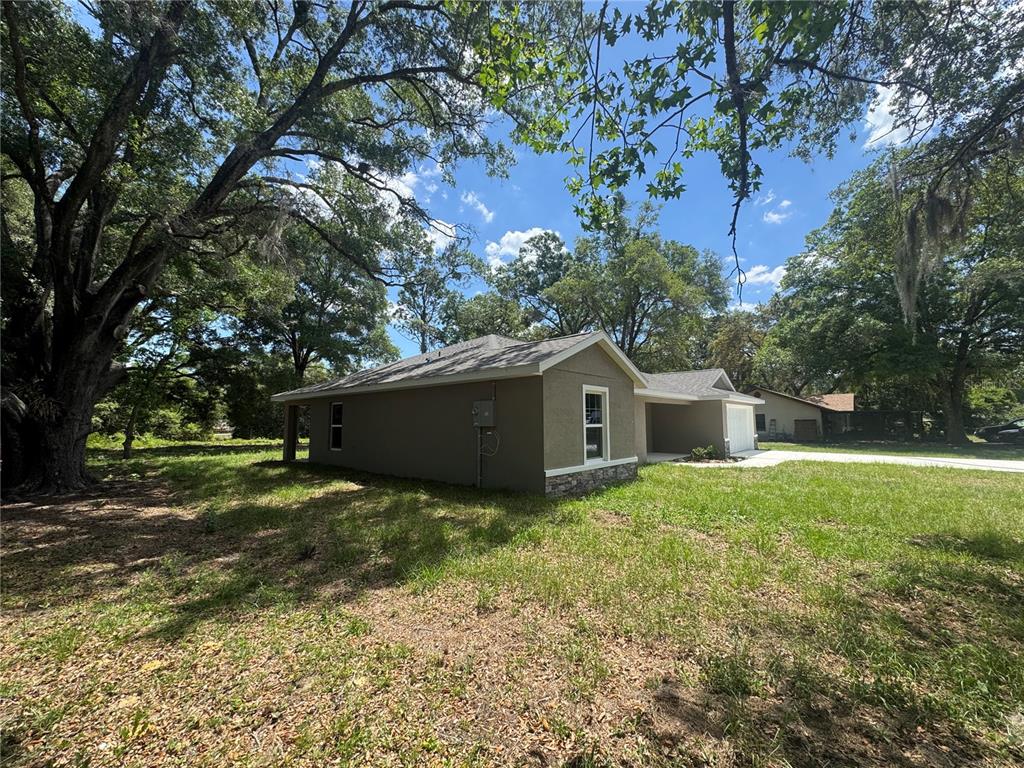 A side view of a single-story house with a tan stucco exterior and stone accents — 8121 SW 202ND TERRACE, DUNNELLON, FL