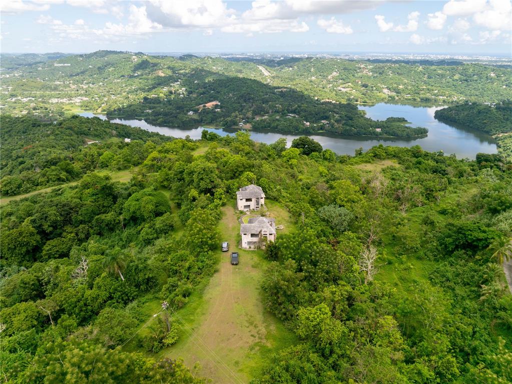 An aerial view shows two houses situated on a grassy hill overlooking a lake — arr 942 JAGUAS, GURABO, PR