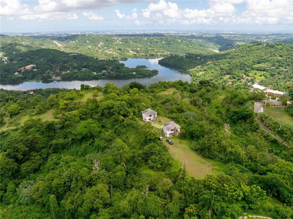 An aerial view shows two houses situated on a lush, green hillside overlooking a lake — arr 942 JAGUAS, GURABO, PR