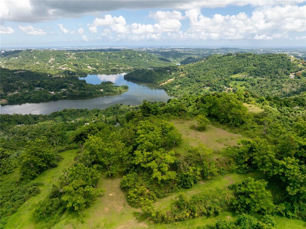 An aerial view shows a grassy hilltop overlooking a lake surrounded by lush green hills — arr 942 JAGUAS, GURABO, PR