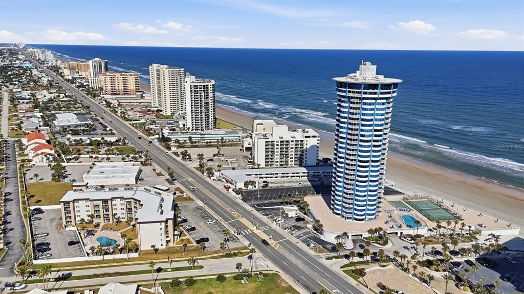 An aerial view shows a tall, cylindrical beachfront tower alongside a coastal road and ocean — 2625 S ATLANTIC AVENUE UNIT 18NW, DAYTONA BEACH, FL