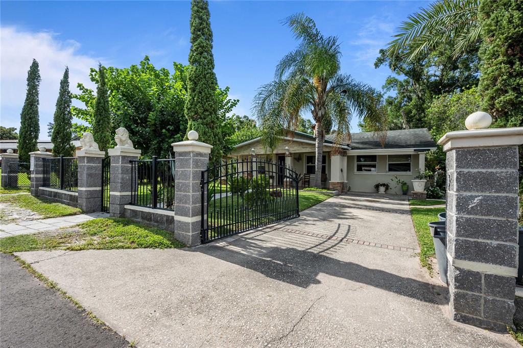 A single-story house with a concrete driveway, gated entrance, and tall cypress trees — 37253 SAFARI DRIVE, DADE CITY, FL