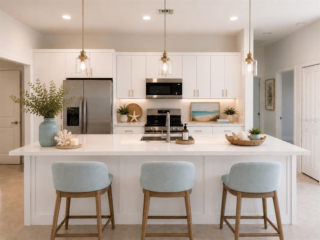 A modern kitchen features white cabinetry, a large island with three stools, and stainless appliances — 2820 W 44 STREET, LEHIGH ACRES, FL