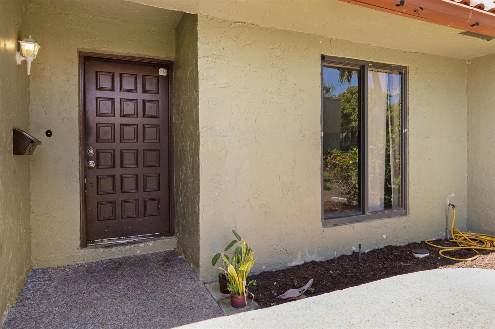 The exterior of a home features a brown paneled door, a window, and a garden bed — 153 SE 7th Street # 1, Deerfield Beach FL 33441, DEERFIELD BEACH, FL