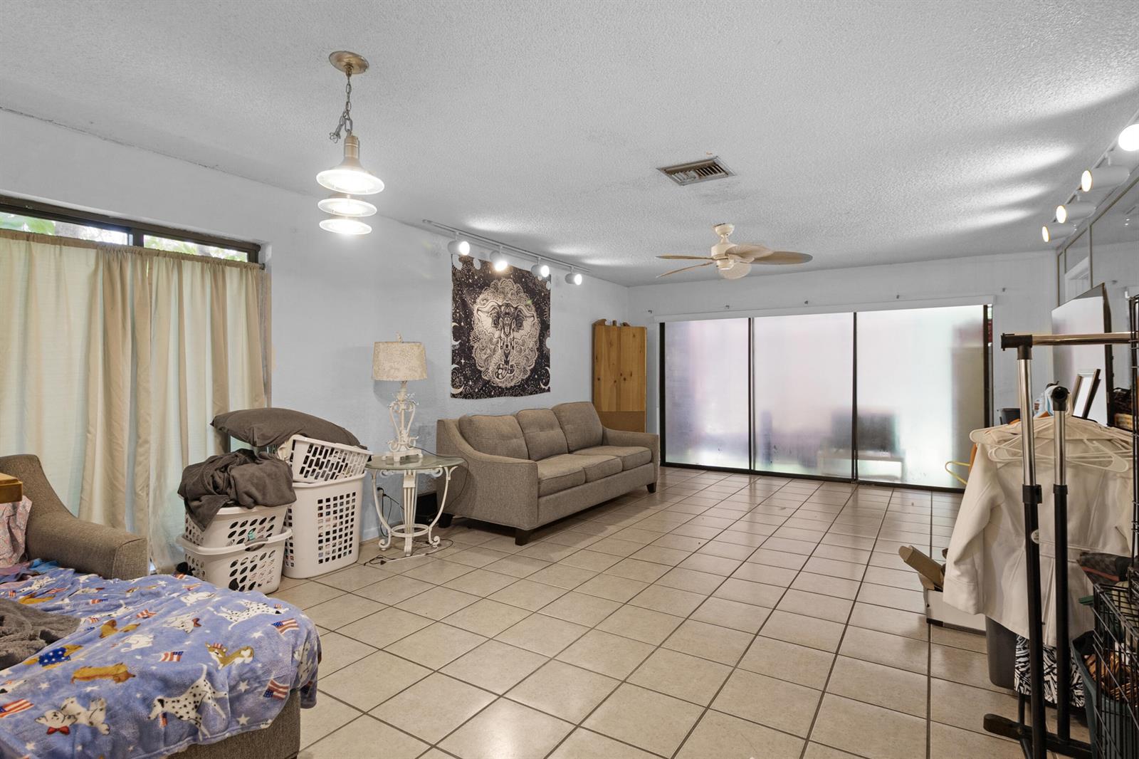 A living room features light-colored tile flooring, a grey sofa, and a large sliding glass door — 153 SE 7th Street # 1, Deerfield Beach FL 33441, DEERFIELD BEACH, FL
